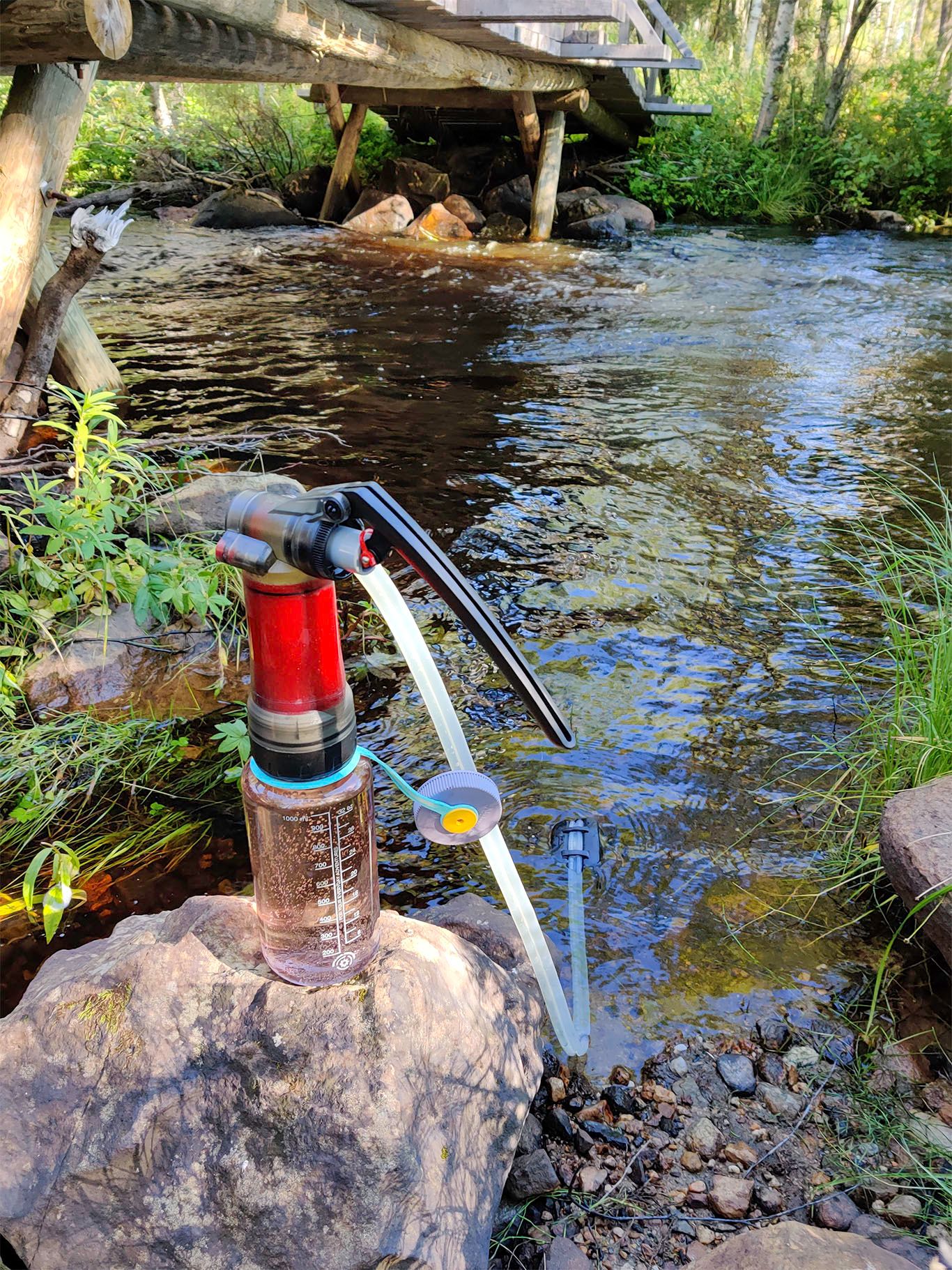 A water purifier extended into the river to pump water to a drinking bottle.
